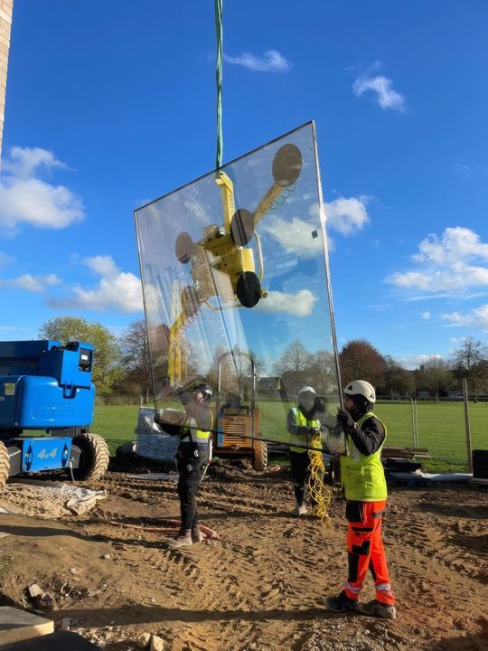 A glazing unit on a vacuum lifter against a blue sky in Cambridge.