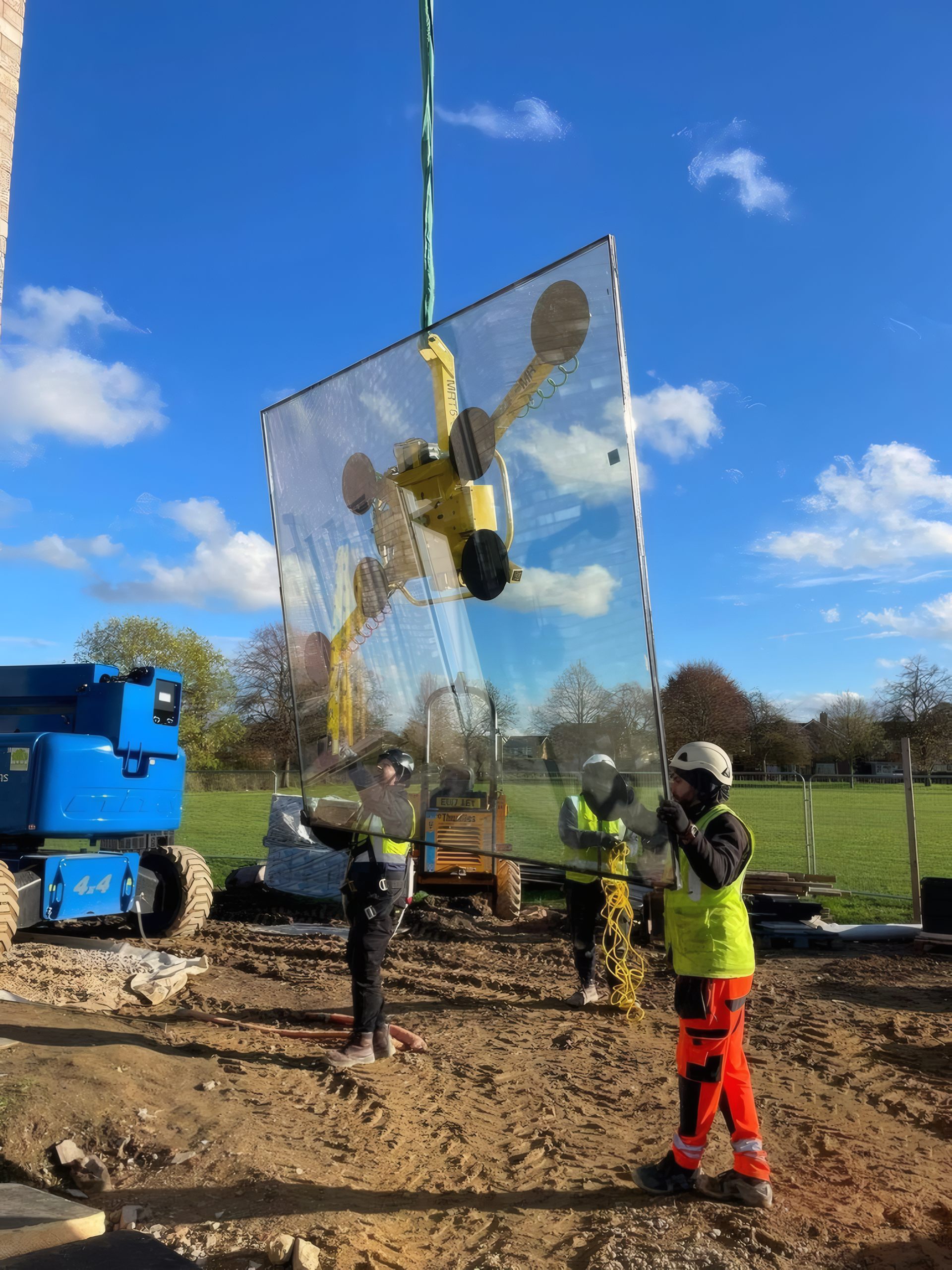 A curtain wall glazing unit on a vacuum lifter, swung against a blue sky by the OMFC team in Cambridge.
