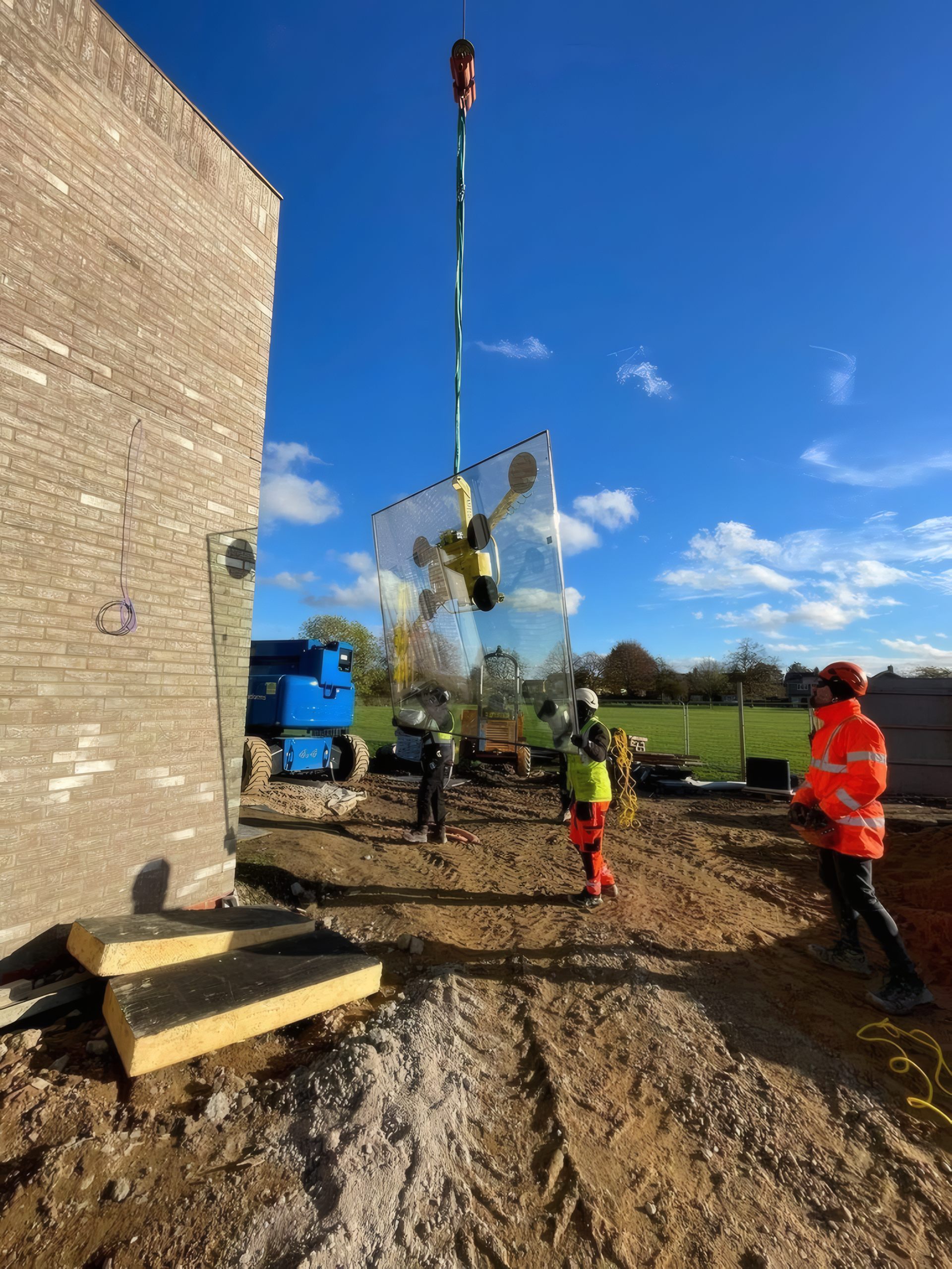A curtain wall glazing unit craned up a brick facade in Cambridge, guided by the OMFC team below.
