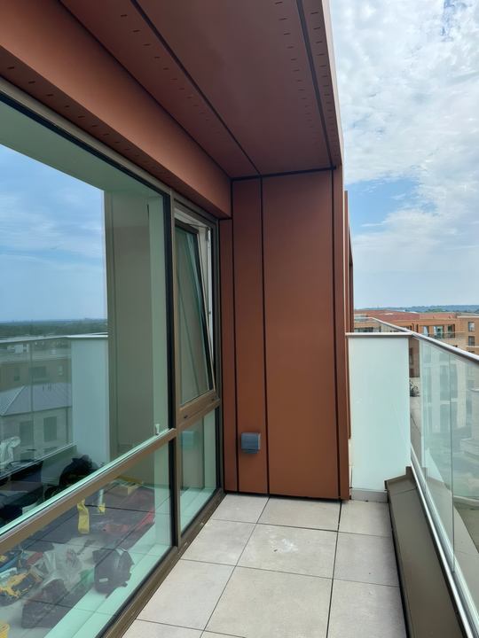 A completed balcony corner with terracotta-finish cladding and a glazed balustrade.